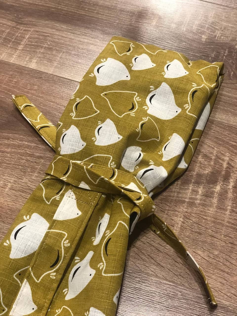 Una tela de color amarillo mostaza con un patrón de pájaros blancos. La tela está atada con una cinta amarilla mostaza.