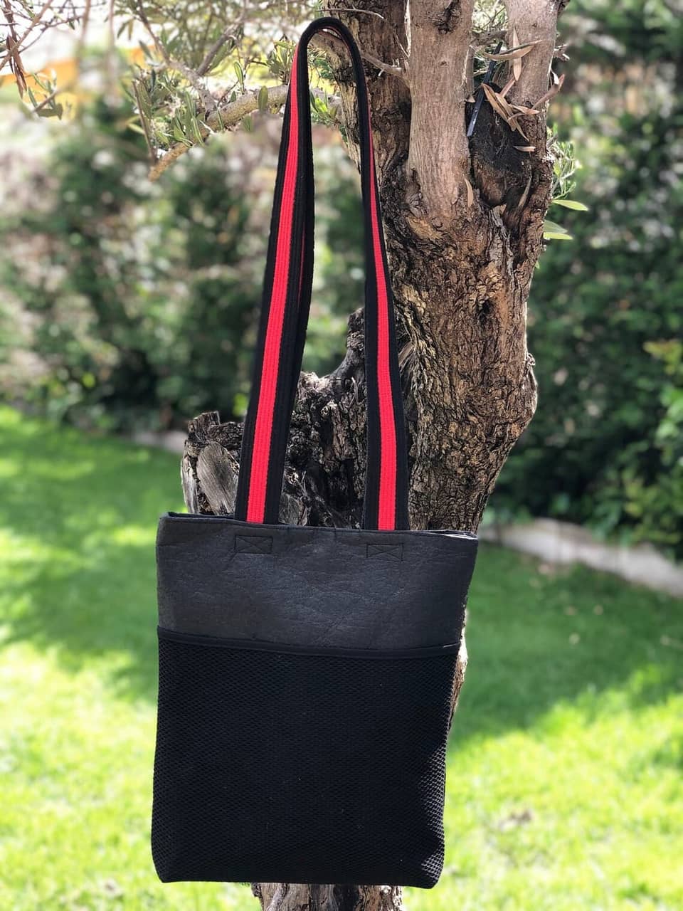 Bolso tote negro con una correa de rayas rojas y negras. El bolso tiene un bolsillo de malla en la parte delantera.